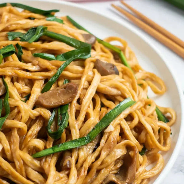 Plate of noodles with mushrooms and green onions on a white plate with chopsticks.